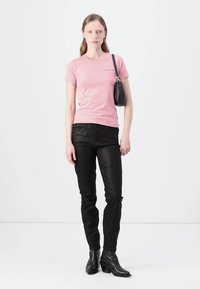 Rózsaszín, rövid ujjú pamut póló, amelyet fekete, slim-fit farmernadrággal viselnek. A modellen fekete kézitáska van, és fekete bokacsizmát visel.