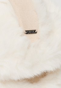 Finta pelliccia color crema con morbida texture, caratterizzata da una fascia in tessuto beige e un'etichetta metallica nera con la dicitura "CEcil."