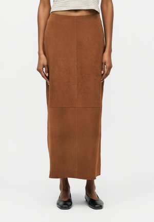 Žena nosi hnedú sukňu s vysokým pásom do členkov, v páre s čiernymi balerínkami a bielym pruhovaným krátkym topom.