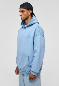 Lichtblauwe hoodie met een gestructureerde capuchon en kangoeroezak. Heeft ribgebreide manchetten en zoom, met een geborduurd logo op de borst.