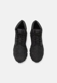 Czarne zamszowe sneakersy z okrągłym noskiem, sznurowane, o teksturowanej powierzchni i gumowej podeszwie z wyraźnym wzorem bieżnika.