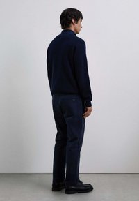 Suéter de punto navy con alto cuello, combinado con pantalones oscuros a juego. El modelo usa botas negras con cordones. Diseño minimalista, textura suave.