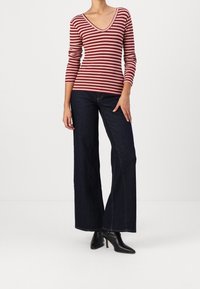 Punainen ja kerma raidoitettu pitkähihainen paita V-pääntiellä, yhdistettynä korkeavyötäröisiin tummansinisiin leveälahkeisiin farkkuihin ja mustiin teräväkärkisiin nilkkakorkoihin.