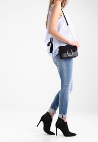 Stivali neri in suede alla caviglia con punta affusolata e tacchi a stiletto, abbinati a jeans skinny blu con effetto usurato e una maglia azzurro chiaro con spalline.