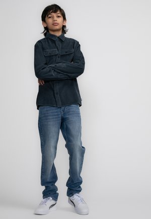 Donkerblauwe corduroy shirt met borstzakken, gecombineerd met lichtblauwe denim jeans en witte sneakers met zwarte accenten.