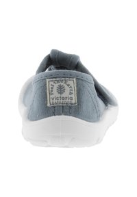 Zapato slip-on de lona azul con suela de goma blanca, con un lazo de tela en la parte posterior y un parche con el logo en el talón.