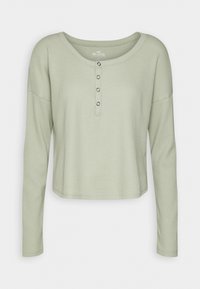 Långärmad, cropped topp i mjukt grönt ribbat tyg med rundad krage och tre knappar fram.