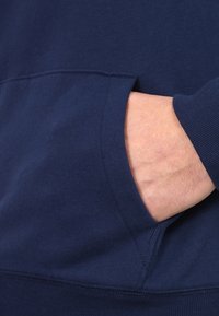 Sudadera azul marino hecha de suave algodón, con un bolsillo tipo canguro. La tela tiene una textura suave con puños acanalados y un dobladillo sin costuras.