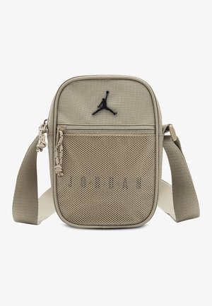 Béžová obdĺžniková crossbody taška s nastaviteľným popruhom, predným sieťovaným vreckom so zipsom a čiernym logom Jumpman v strednej hornej časti.