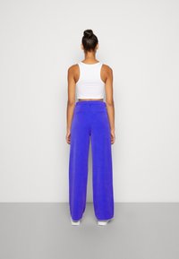 Pantalons larges en tissu bleu vif, avec une texture lisse et deux poches arrière, associés à un débardeur court blanc.