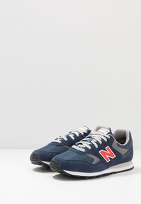 Námořnické modré semišové a síťované tenisky s šedým akcentem a výrazným červeným logem. Mají bílou mezipodešev a černou gumovou podrážku.