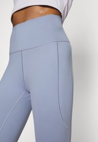 Světle modré legíny s vysokým pasem vyrobené z elastické látky, s plochými švy a bočním kapsou pro úložný prostor.