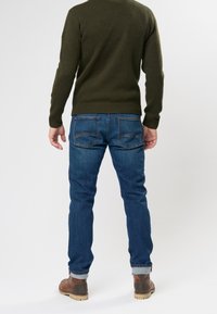 Pull vert foncé en maille avec poignets côtelés, assorti à un jean denim bleu avec poches arrière et ourlets retroussés, porté avec des bottes marron.