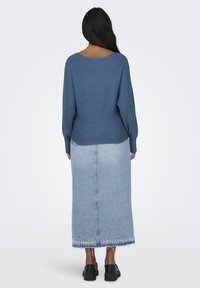 Pull en tricot bleu à côtes avec un encolure large, associé à une jupe maxi en denim bleu clair avec un ourlet brut. Des chaussures à plateforme noires complètent le look.
