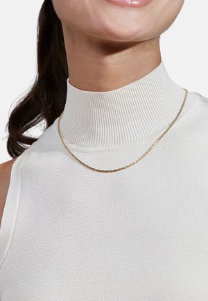 Collana a catena d'oro con design intrecciato indossata sopra un top bianco a collo alto e a coste, che mostra una texture liscia e una lucentezza sottile.