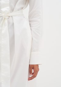 Weißes Baumwollhemdkleid mit einem Bindegürtel, langen Ärmeln und glatter Textur. Verfügt über einen sauberen Kragen und geknöpfte Manschetten.