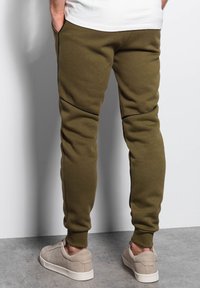 Olivgrüne Jogginghose aus weichem Stoff, mit schlanker, taillierter Passform, seitlichen Taschen und kontrastierenden schwarzen Nähten.