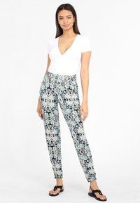 Rakstainas bikses gaiši zilā, melnā un baltā krāsā; pieguļoša forma ar potītes aprocēm; kombinētas ar baltu V-veida kakla topu un melnām sandālēm.