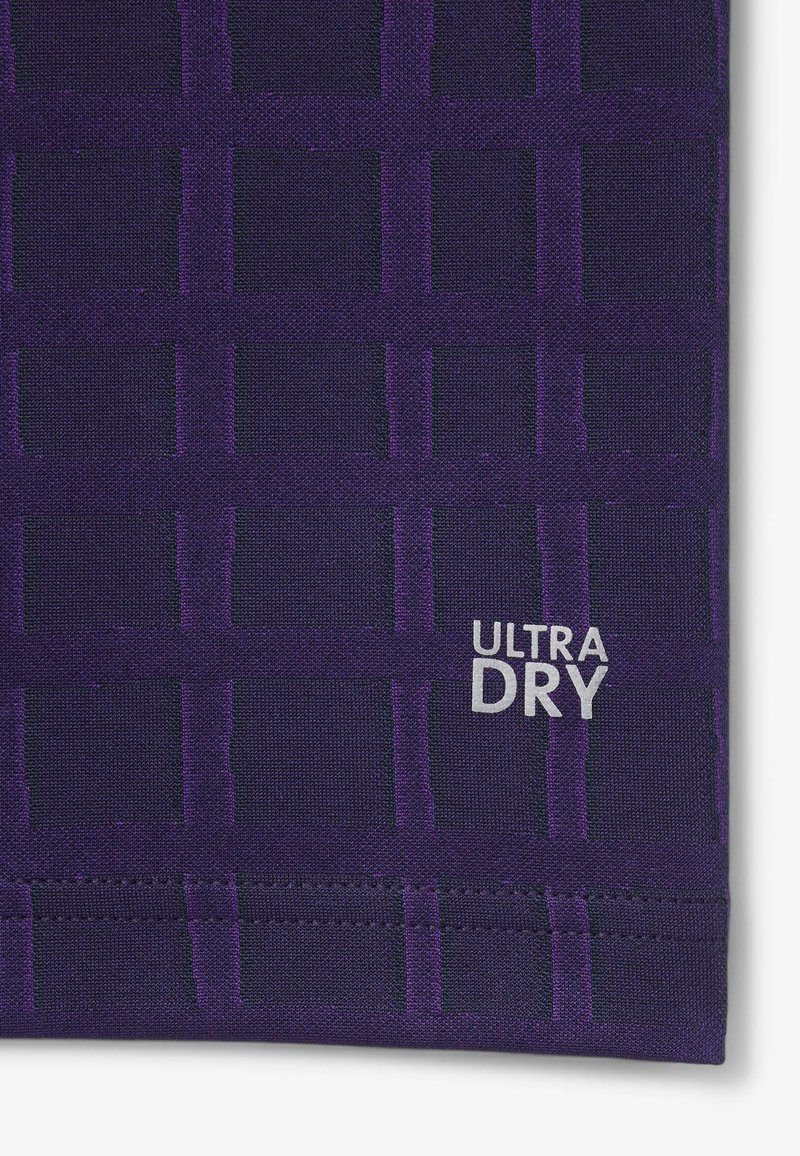 Tessuto viola con una trama a griglia, caratterizzato da una finitura testurizzata. Include un'etichetta argento "ULTRA DRY" nell'angolo in basso a destra.