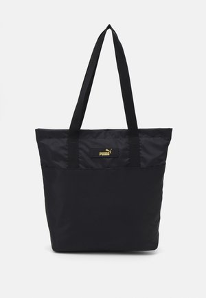 Borsa tote nera realizzata in tessuto resistente con doppi manici neri. Presenta una targhetta con logo dorato sul davanti, design minimalista.