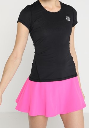 Woman wearing a fitted black short-sleeve top with a small logo and a bright pink flared skirt against a plain background.