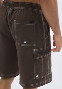 Hnedé cargo šortky s bielym prešitím, elastickým pásom, dvoma bočnými vreckami a zadným vreckom s logovou nášivkou.