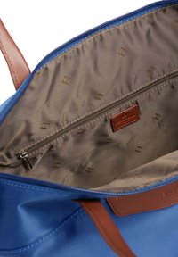 Interno di una borsa di tessuto blu con una fodera color cammello, dotata di una tasca con zip e logo impresso. Le cinghie in pelle marrone aggiungono un contrasto.