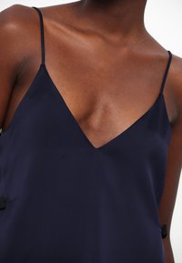 Camisole bleu marine avec un décolleté en V profond, des bretelles fines et une texture lisse et soyeuse avec des accents noirs sur les côtés.