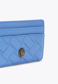 Jasnoniebieski skórzany etui na karty z pikowanym wzorem, z ozdobnym złotym akcentem w kształcie dłoni. Trzy kieszonki na karty.