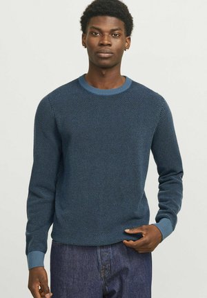 Gebreide blauwe trui met een textuurpatroon, ronde hals en geribde manchetten. Gecombineerd met donkerblauwe jeans.