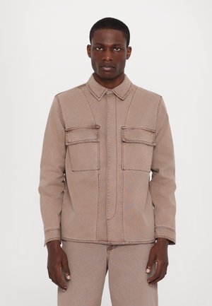 Beige denim jacket with a collared neck, featuring two chest pockets, visible stitching, and a front button closure. Smooth texture.