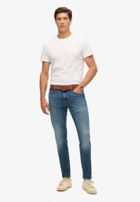 Camiseta de algodón blanca combinada con jeans de mezclilla azul claro. Cinturón de cuero marrón, zapatillas beige. Diseño minimalista con un ajuste relajado.