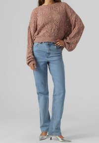 Vaaleanpunainen neule cropped neuletakki, jossa on teksturoitu kuvio, yhdistettynä vaaleansiniset korkeavyötäröiset farkut ja hopeiset kärjelliset korkokengät.