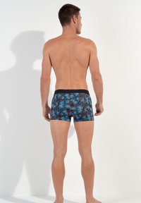 Badeshorts mit schwarzem Grund, verziert mit lebhaften tropischen Blattmustern in Blau und Rot. Elastischer Bund, enganliegendes Design, Länge bis zur Mitte des Oberschenkels.