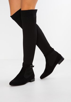 Nogi w czarnych prążkowanych zakolanówkach oraz czarnych krótkich botkach z małym paskiem na klamrę.