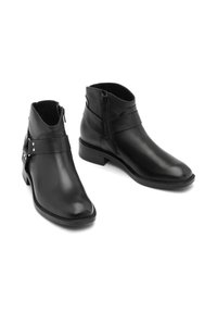 Botas negras de cuero hasta el tobillo con punta afilada, cierre de cremallera lateral y correas decorativas con tachuelas en el tobillo exterior. Tacón bajo tipo bloque.