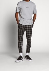 Harmaa lyhythihainen t-paita, jossa pieni kirjailtu yksityiskohta. Mustavalkoiset ruudulliset suorat housut, kapealla leikkauksella, yhdistettynä mustiin lenkkareihin.