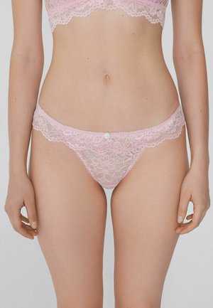 String en dentelle rose avec un motif floral, des bords festonnés et un petit bouton à l'avant. Texture douce et délicate. Illustre un design complexe.