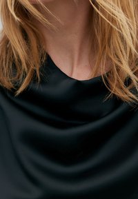 Haut en satin noir doté d'un décolleté drapé. Le tissu semble lisse avec un léger éclat et une texture douce, créant des plis délicats.