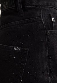 Pantalones de mezclilla negra con cuentas negras decorativas esparcidas por la tela. Incluye una pequeña etiqueta con el logo en el bolsillo.