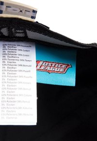 Crni tekstilni etiketa s plavom oznakom koja prikazuje "Justice League" logo, s popisom sastava materijala: 63% poliestera, 34% pamuka, 3% elastana.