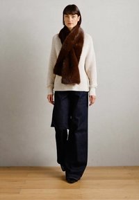 Oversized cream sweater paired with wide-leg dark denim trousers. A fluffy brown scarf is draped around the neck for added warmth.