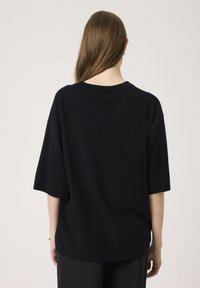 Sort kortærmet sweater med en afslappet pasform, rund halsudskæring og ribbede kanter. Glat tekstur, minimalistisk design, ingen synlige mønstre eller hardware.