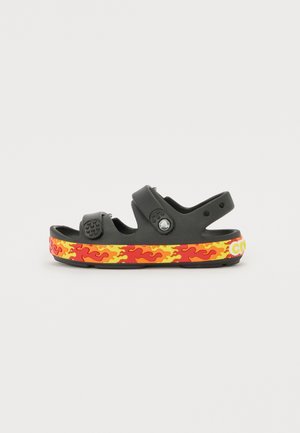 Sandálias pretas com tiras ajustáveis, um topo texturizado e uma sola com padrão de chamas em vermelho e amarelo vibrantes. Embelezadas com detalhes circulares.