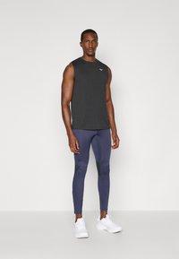 Top atlético sin mangas negro combinado con leggings de compresión azul marino con detalles de malla negra. Zapatillas deportivas blancas completan el look.
