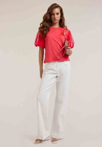 Top rojo de manga corta con mangas de tul y detalle floral, combinado con pantalones de pierna ancha blancos y tacones con tiras.