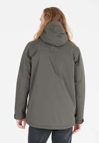 Giacca impermeabile grigia con cappuccio, caratterizzata da una superficie liscia, polsini elasticizzati e un taglio dritto. La vista posteriore mostra un design minimalista.