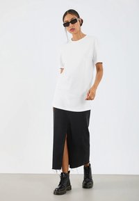 Bílé tričko s kulatým výstřihem spojené s černou džínovou sukní s předním rozparkem a roztřepeným lemem, doplněné černými šněrovacími botami.