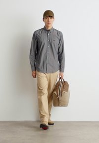 Camisa gris de botones, pantalones beige y un bolso marrón claro. La gorra tiene un visera curvada. Diseño sencillo, colores neutros y texturas suaves.