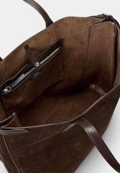 Sac fourre-tout en suède marron avec des poignées en cuir, doté d'une poche zippée et de compartiments ouverts. Texture douce avec un design minimaliste.